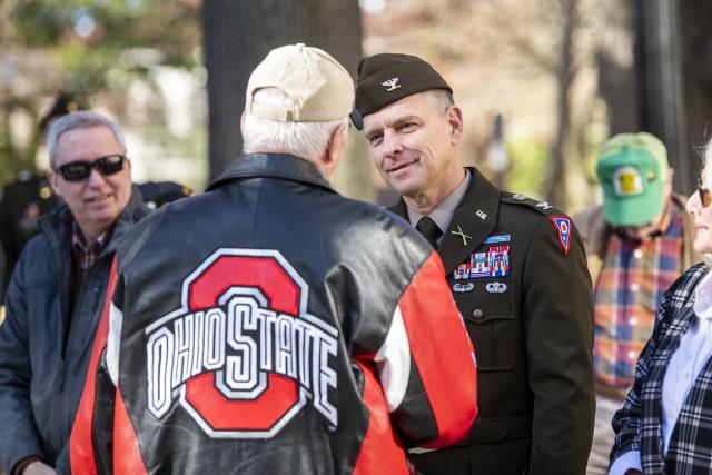 An older gentleman in a Block O coat greets a middle aged man in uniform on campus.
