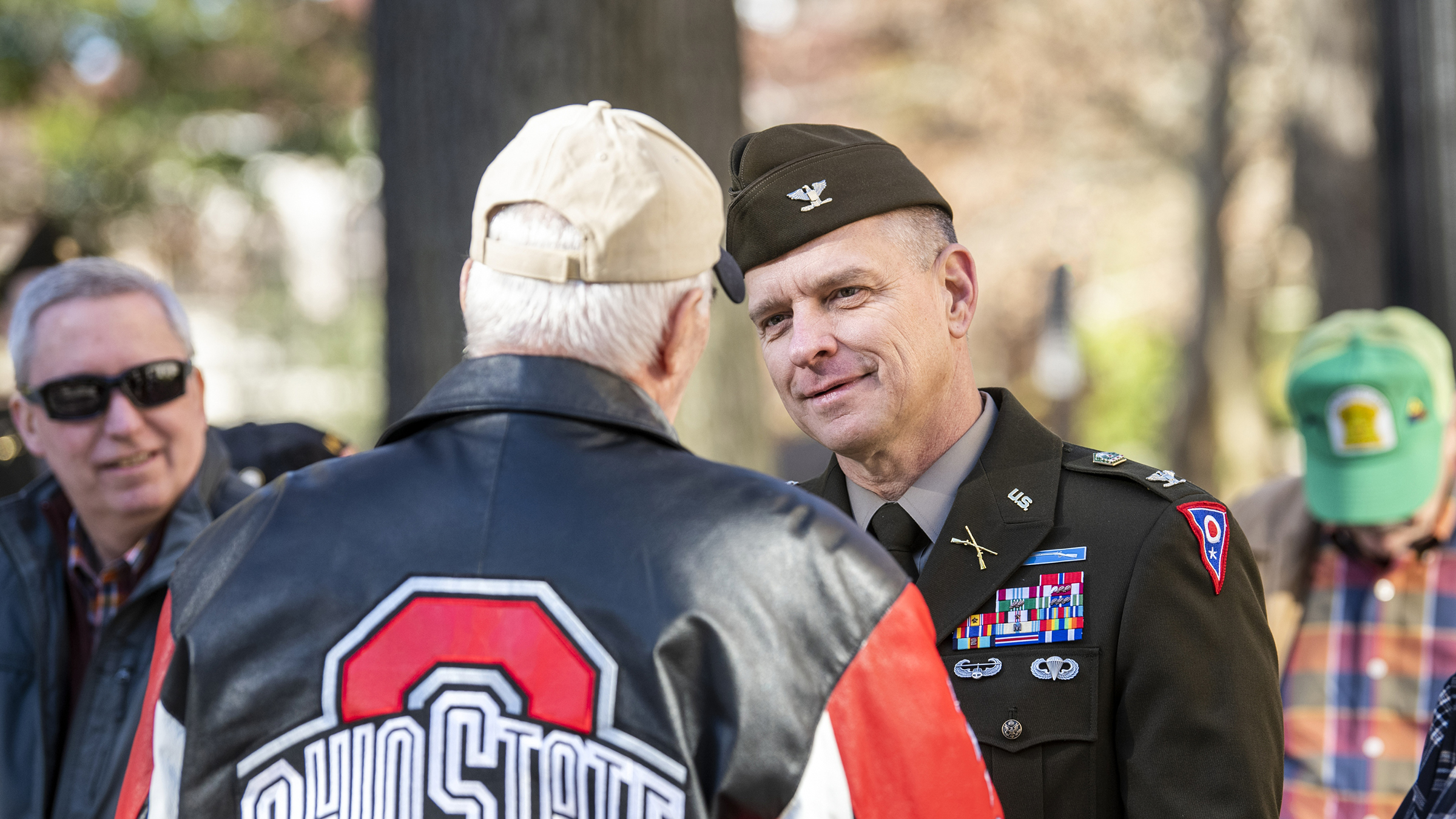 Two people shaking hands, one wearing military attire and the other in an Ohio State leather jacket
