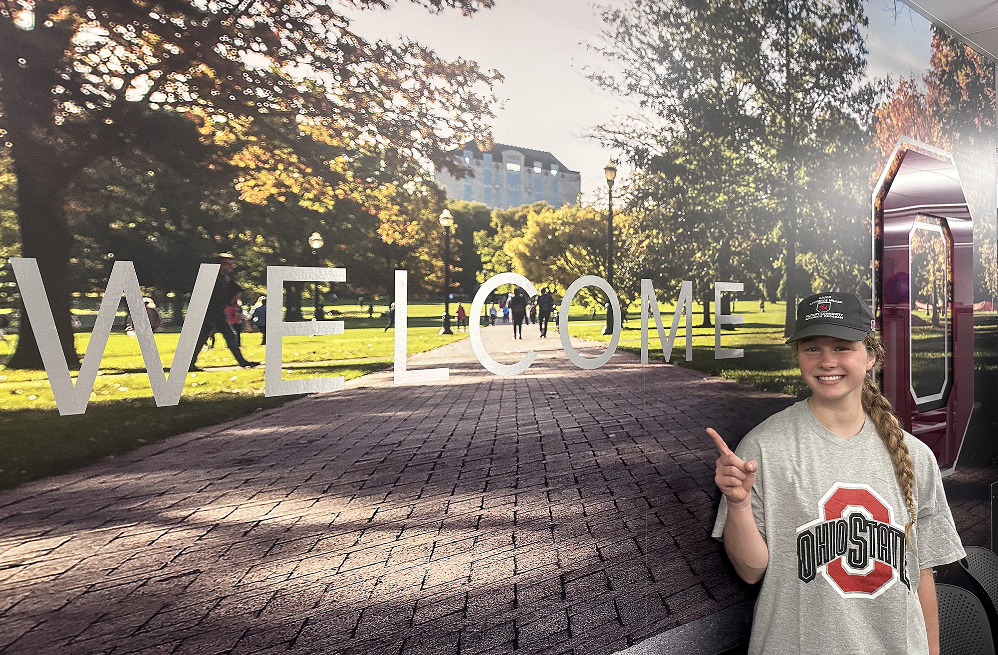 Student wearing pointing to a welcome sign while wearing a shirt with an Ohio State logo on it