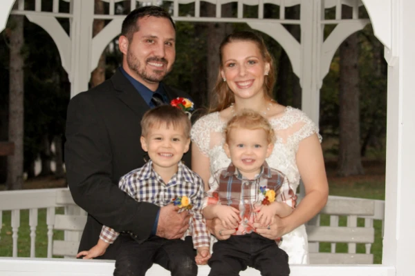 Candid picture of Jesse Glass, his wife, and two children all formally dressed in front of a Gazebo.