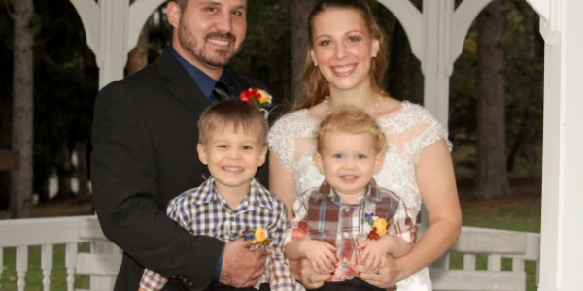 Candid picture of Jesse Glass, his wife, and two children all formally dressed in front of a Gazebo.