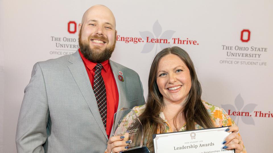 Two people smiling at the camera with one holding an award and a certificate